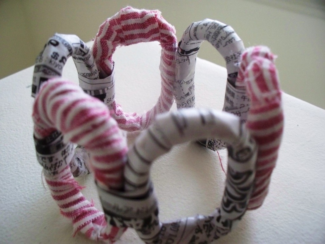 Ett handgjort armband av återvunnet tygmaterial med rosa randiga och tidningstryckta cirkulära länkar.